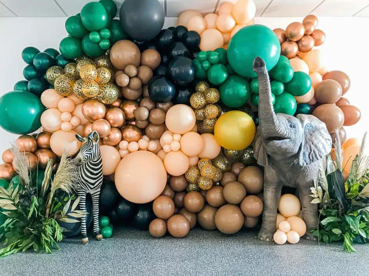 an elephant and zebra are standing in front of a wall of balloons and jungle plants and a zebra is standing in front of the balloon wall