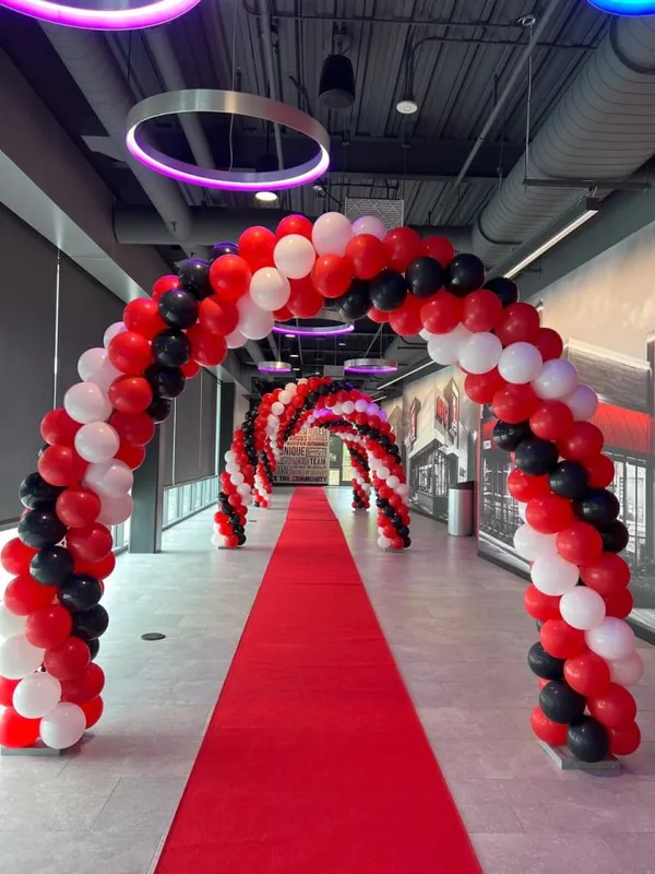 A large, red carpeted hallway is decorated with a large archway made of red ribbons and balloons, creating a festive atmosphere.