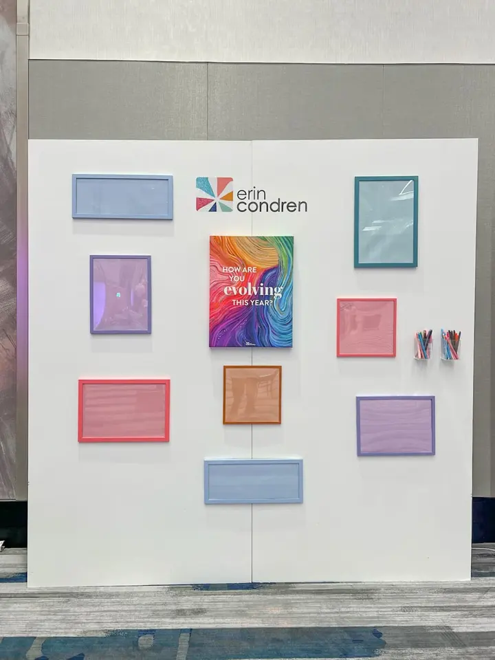 A white wall display featuring various colorful frames, including the Erin Condren logo, and a book titled "Evolving the Mind".