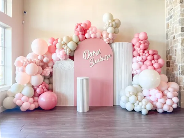 The image features a large pink and white balloon-filled room with a pink and white sign that reads "Happy Birthday."