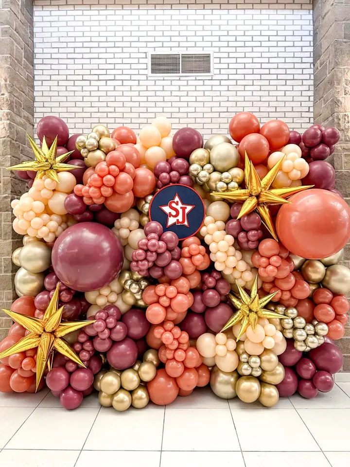 A vibrant display of various colorful fruits, including grapes, tomatoes, and starfruit, arranged in an artistic composition against a plain white brick wall background.