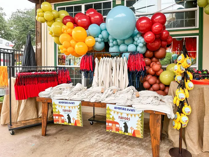 A vibrant and colorful display of balloons, clothing, and other merchandise arranged in an eye-catching manner in front of a building.