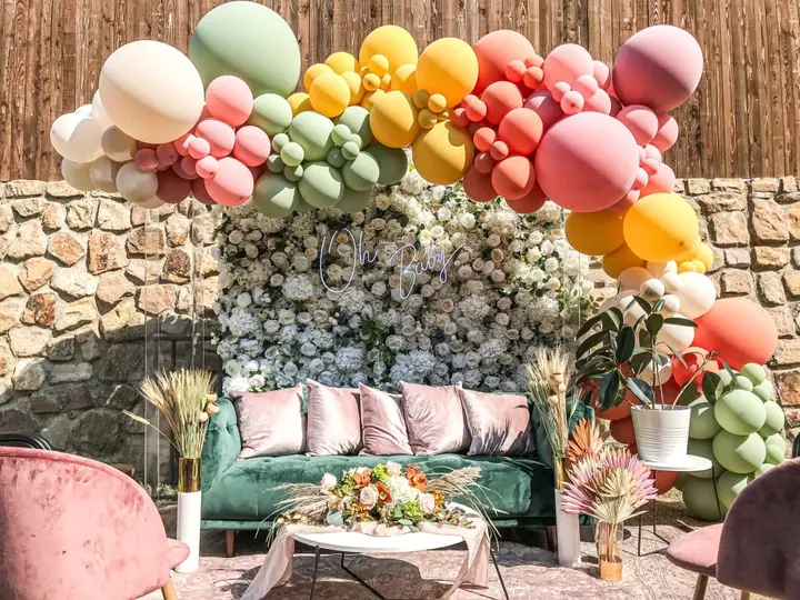 A vibrant and whimsical outdoor setting featuring a cozy seating area surrounded by a colorful array of balloons and lush greenery, creating a festive and inviting atmosphere.