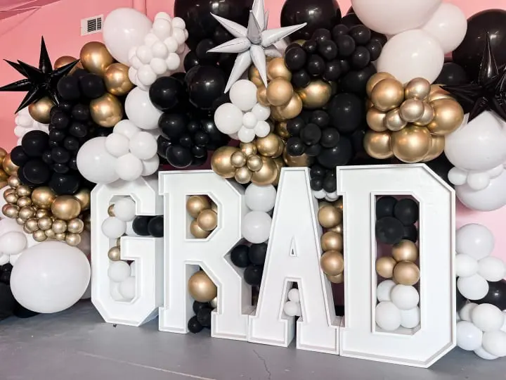 a large group of balloons that spell out the word grad in front of a backdrop of black, white, and gold balloons
