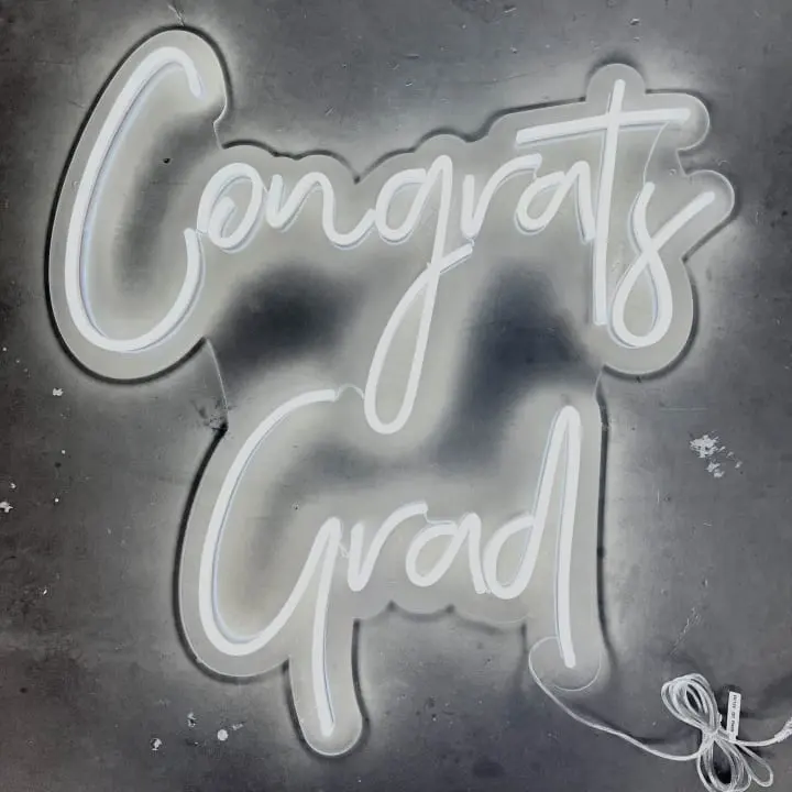 a neon sign that says congrats and grad on a gray background with a bow on the bottom of the sign