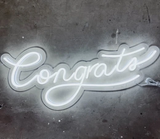 a neon sign that says congrats on a concrete wall with a chain hanging from it's side