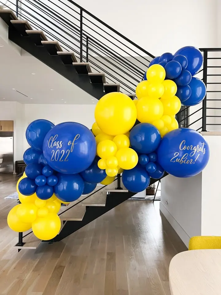 a bunch of blue and yellow balloons are on the stairs of a staircase leading up to the second floor of a house