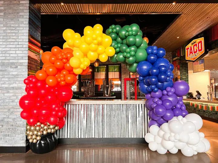a bunch of balloons that are on the ground in front of a store front entrance with a rainbow colored balloon arch in the middle of the entrance