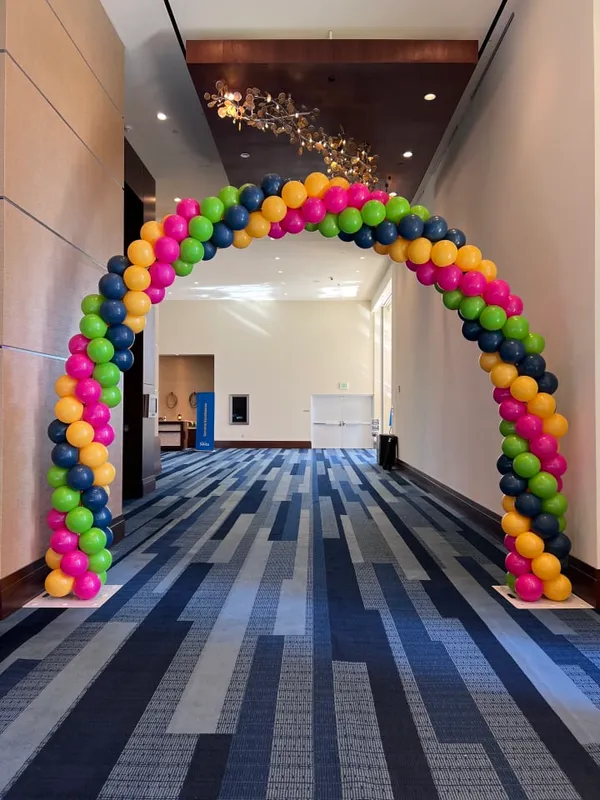 The image features a large, colorful archway made of balloons in a hallway, creating a festive atmosphere.