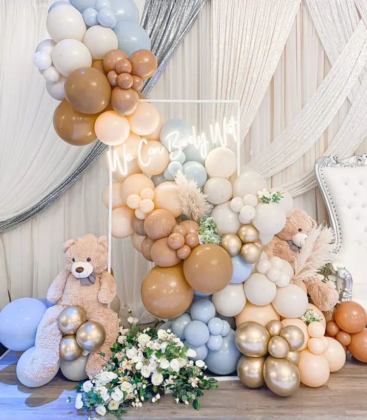a table topped with balloons and a teddy bear next to a sign that reads welcome to our baby on it