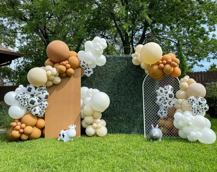a bunch of balloons that are on the ground in the grass near a fence with a dog on it