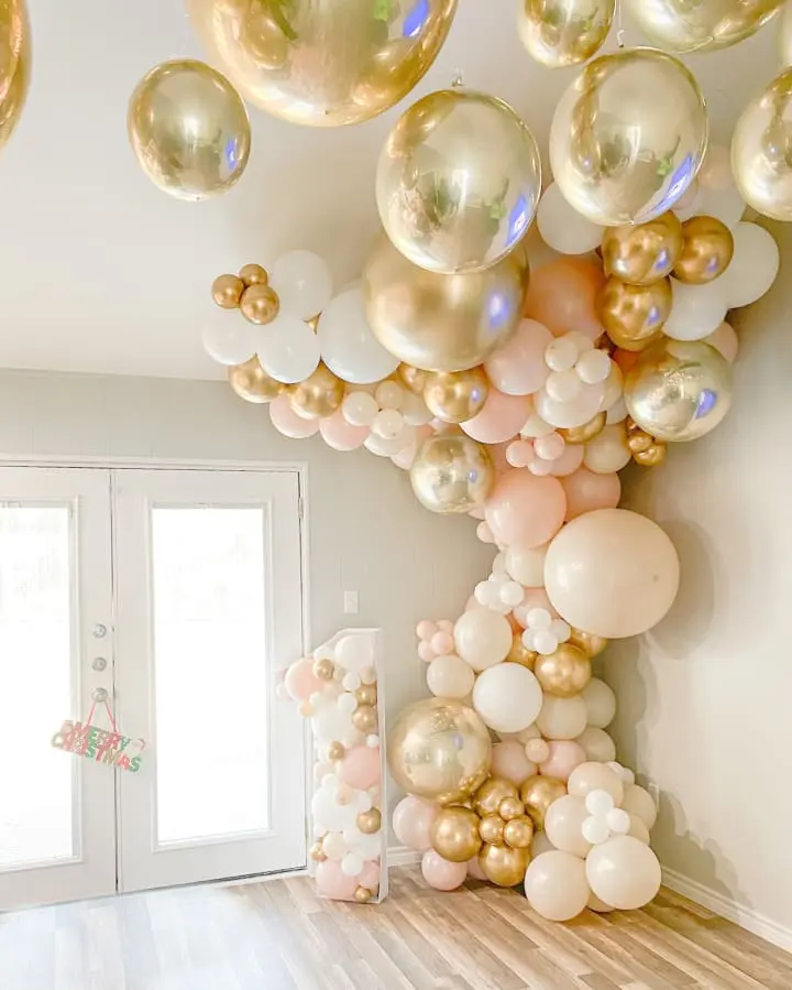 a room filled with lots of balloons and a bunch of white and gold balloons hanging from the ceiling of the room