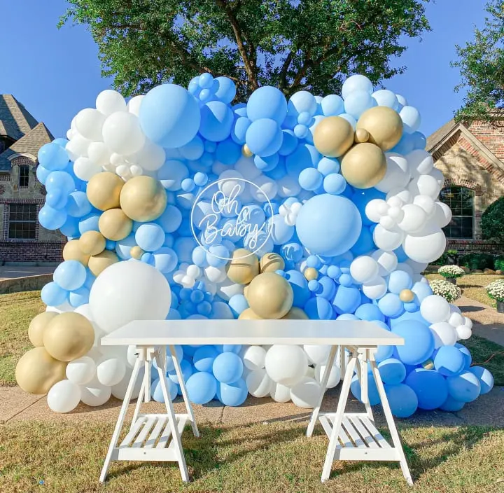 a blue and gold balloon backdrop with a white table and white folding chairs in front of a large blue and gold balloon backdrop