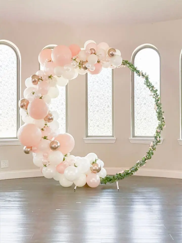 a balloon arch in a living room with a round balloon arch in the middle of the room with balloons and greenery on the top of the arch