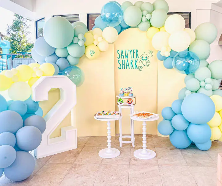 a table with a cake and balloons in the shape of numbers on the wall and a table with a cake on the table in the middle of the room