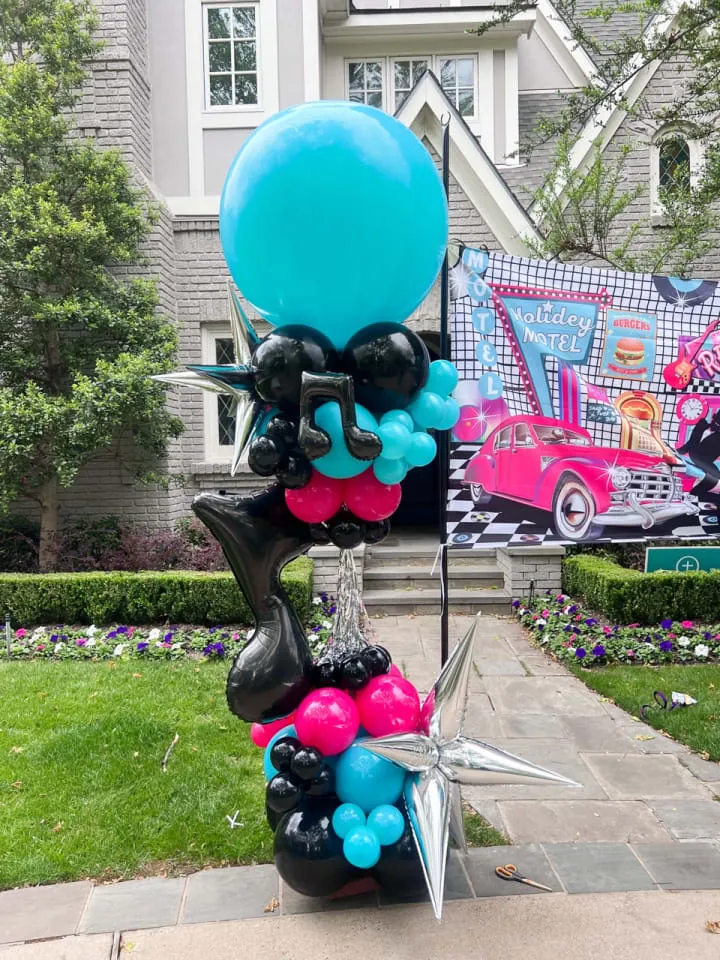 a bunch of balloons that are sitting on a pole in front of a house with a car in the background