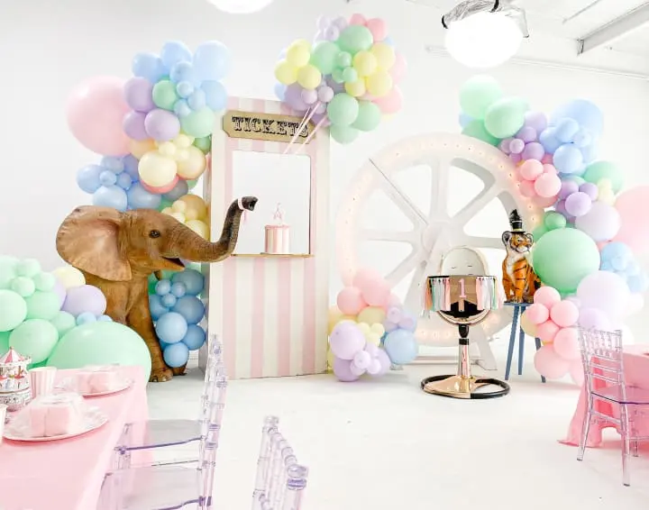 an elephant is standing in a room with balloons on the wall and a table with chairs and a mirror