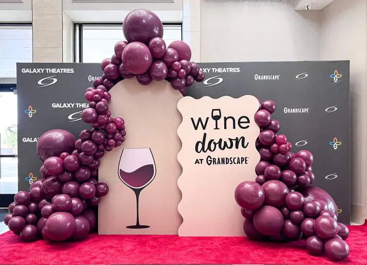 a table with balloons and a wine sign on it with a glass of wine in the middle of the table