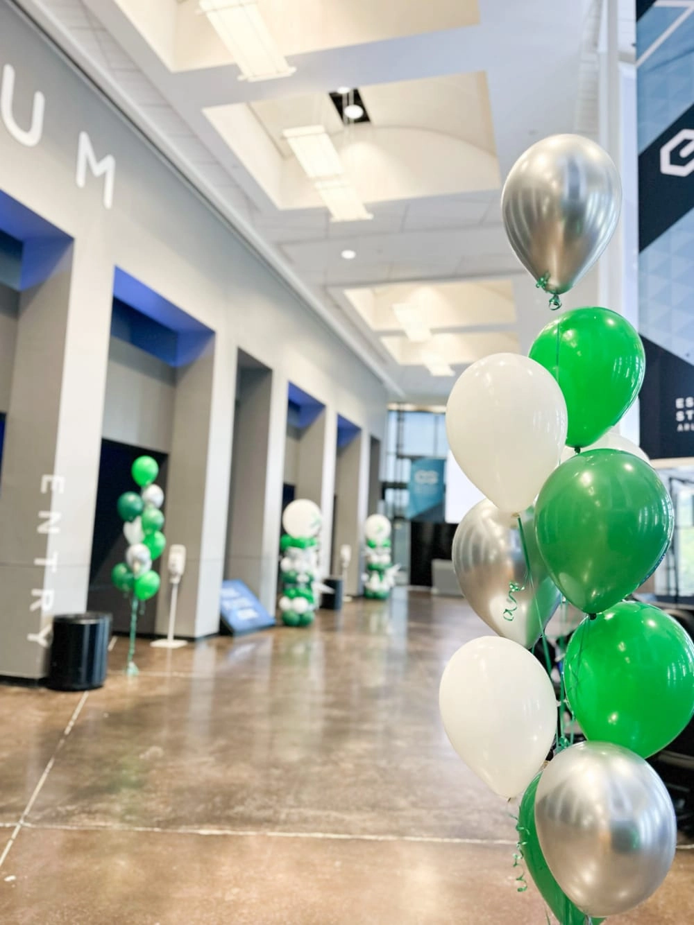 The image shows a hallway decorated with green and white balloons, with a tiled floor and walls in the background.