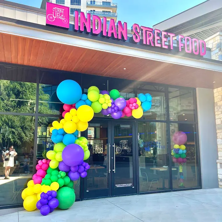 a building with a sign that says indian street food on it and balloons in the front of the building