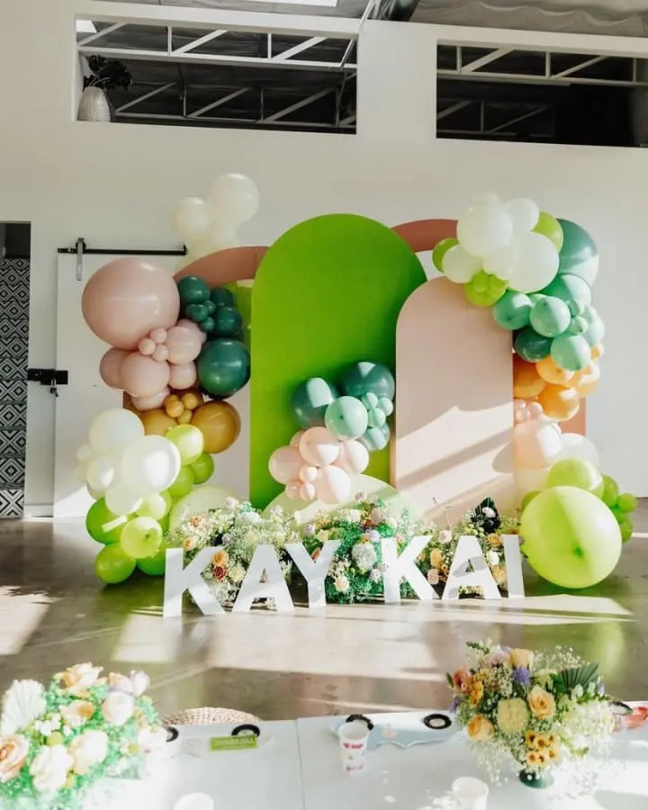 a table topped with balloons and a sign that says kayka on the side of the table with flowers and greenery on the side of the table