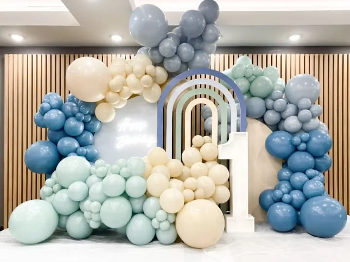 a large balloon arch with blue, white, and grey balloons on top of a table in a room