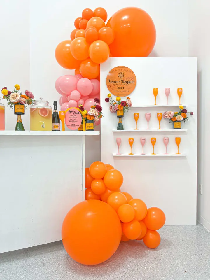 a bunch of orange balloons sitting on top of a white counter next to a shelf filled with bottles and glasses
