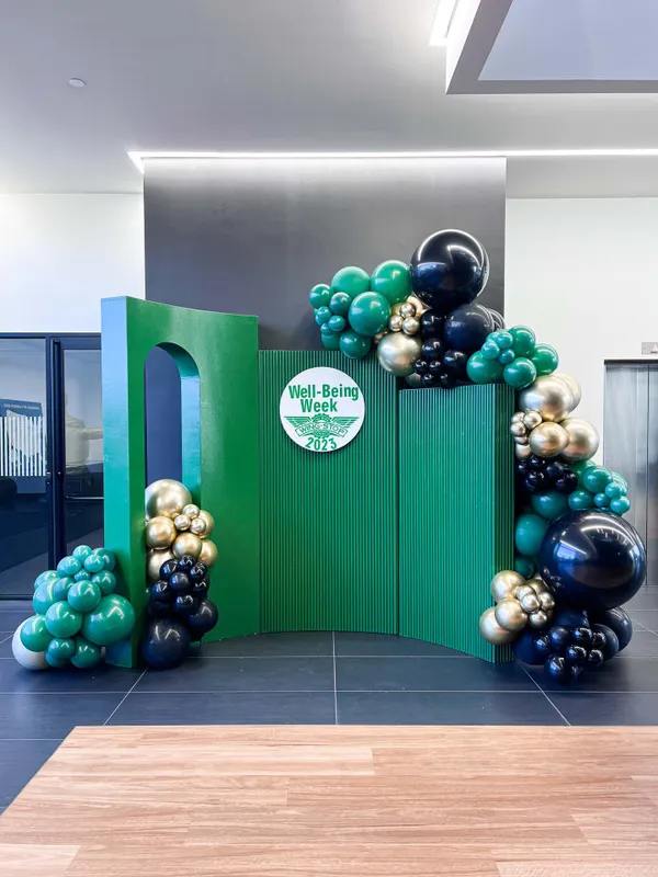 The image features a large green and white sculpture of a Christmas tree with a variety of balloons