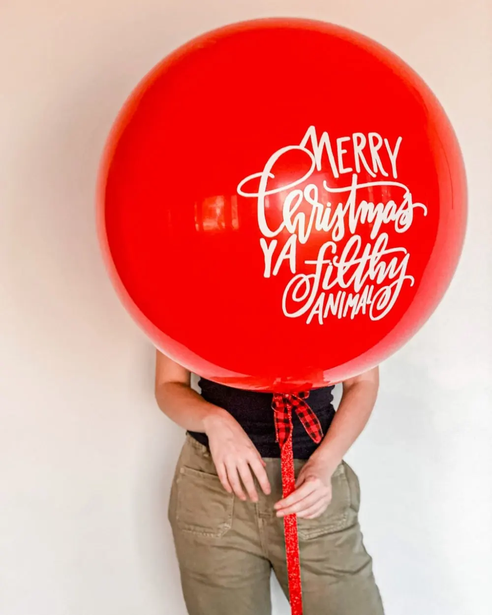 a woman holding a red balloon with a merry christmas message on it's side and a red ribbon around her neck