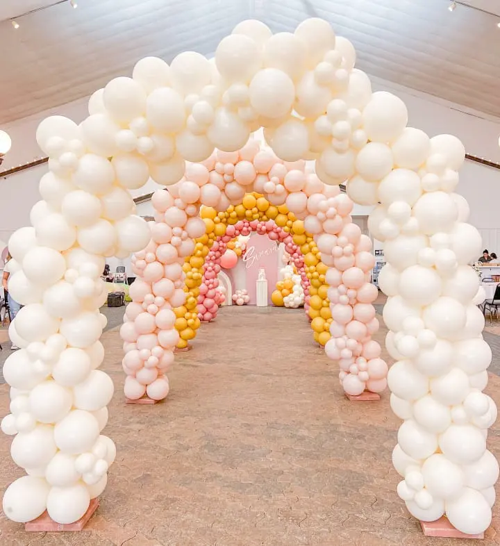 a large arch made out of balloons in a room with a table and chairs in front of the arch