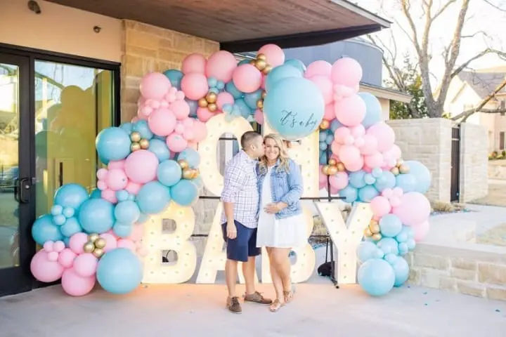 a man and a woman standing in front of a large balloon sign with the word baby written on it