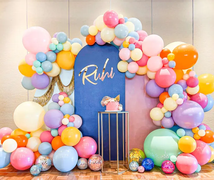 a birthday party with balloons and a cake on a table with a backdrop of balloons and a cake on a stand