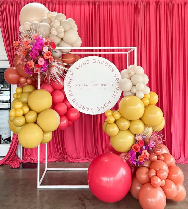 a bunch of balloons and a sign on a stand in front of a red curtain and a pink curtain