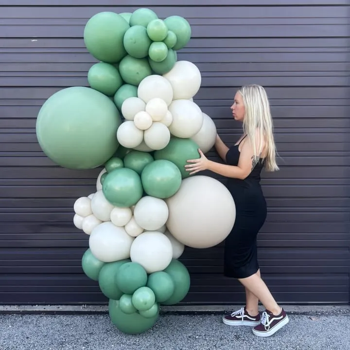 a woman is standing next to a giant balloon sculpture that has green and white balloons attached to it, and is leaning against a garage door