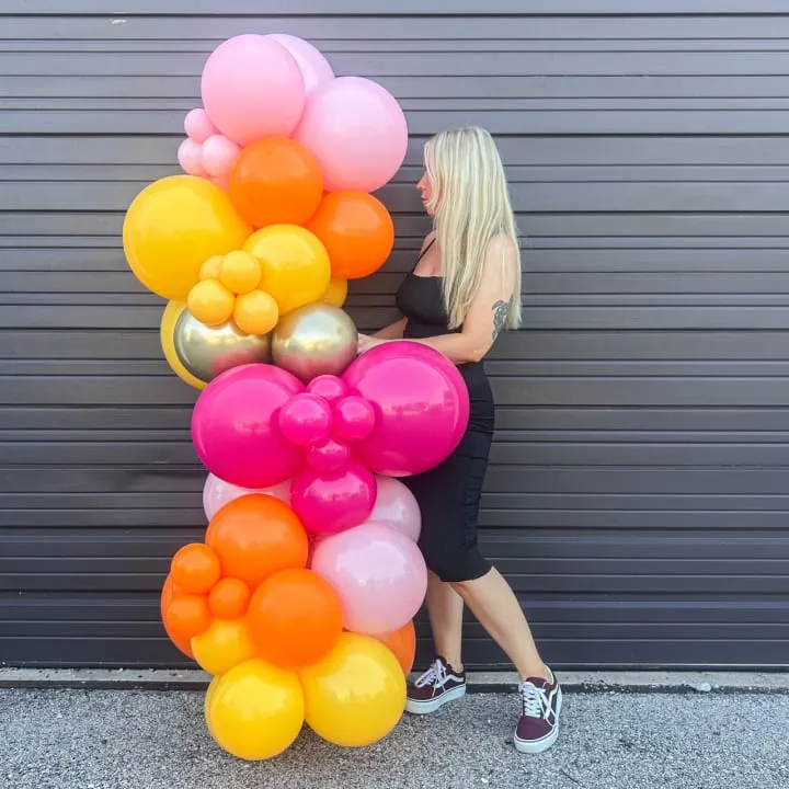 a woman standing in front of a garage door with a 6 ft balloons garland