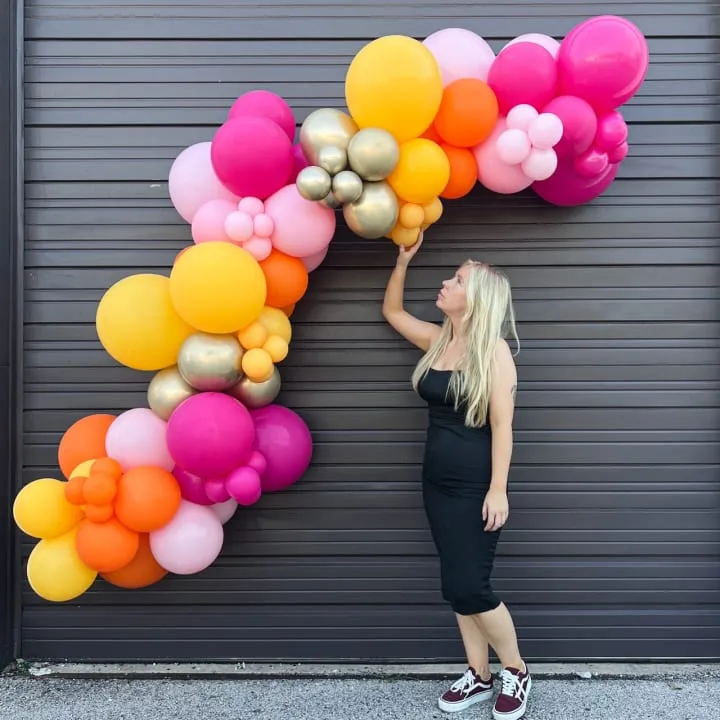 a woman standing in front of a garage door with a 10 ft balloons garland