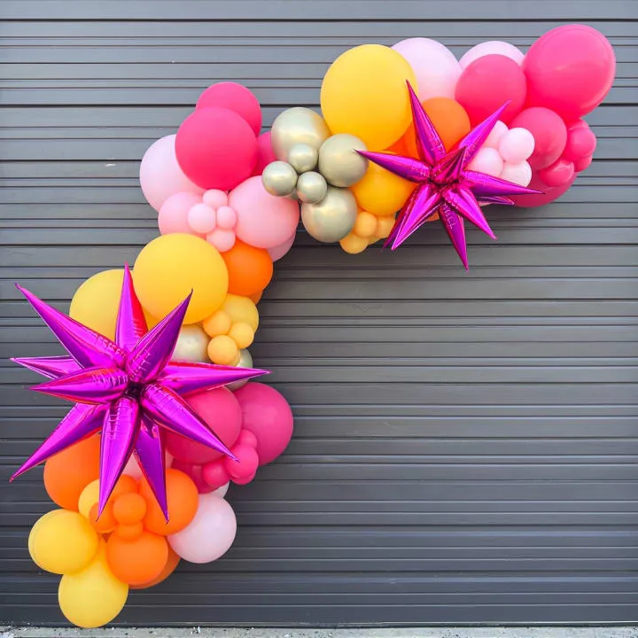 a wreath made out of balloons and starbursts on a garage door with a purple ribbon tied to it