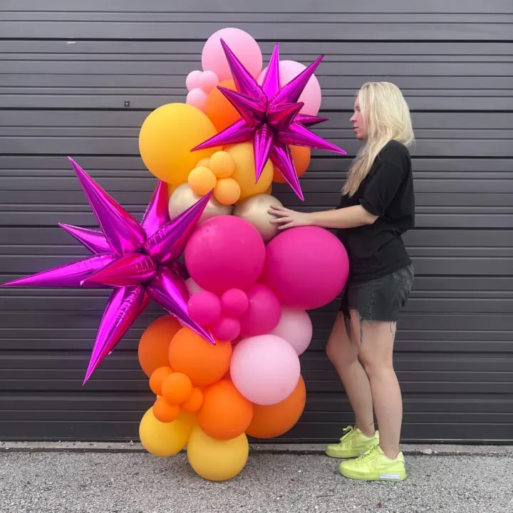 a woman standing with a 6 ft balloons garland and starbursts