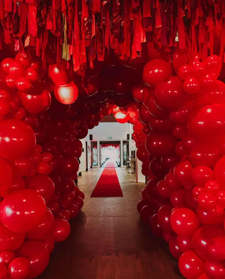 a hallway with red balloons and streamers hanging from the ceiling, and a red carpet on the floor