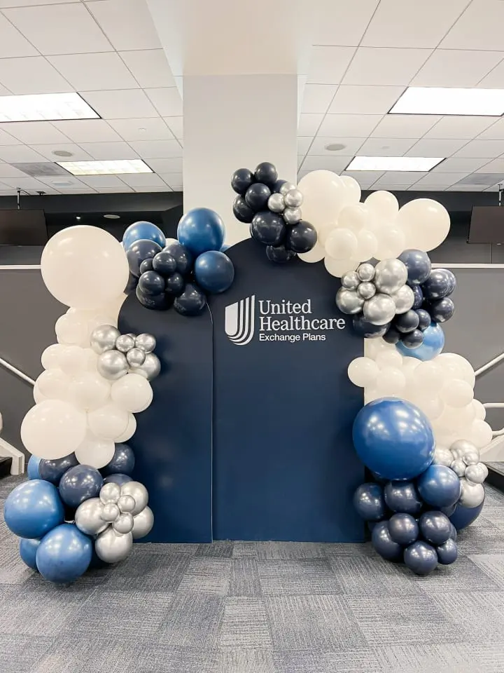 a large balloon arch in an office lobby decorated with blue, white and silver balloons and a sign that reads united healthcare