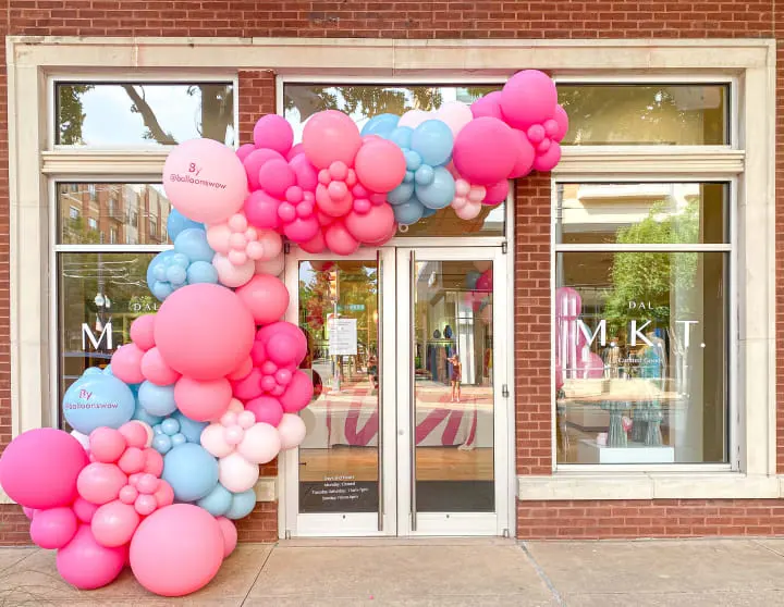 a bunch of balloons that are in front of a store front door that is decorated with a pink, blue, and pink balloon arch