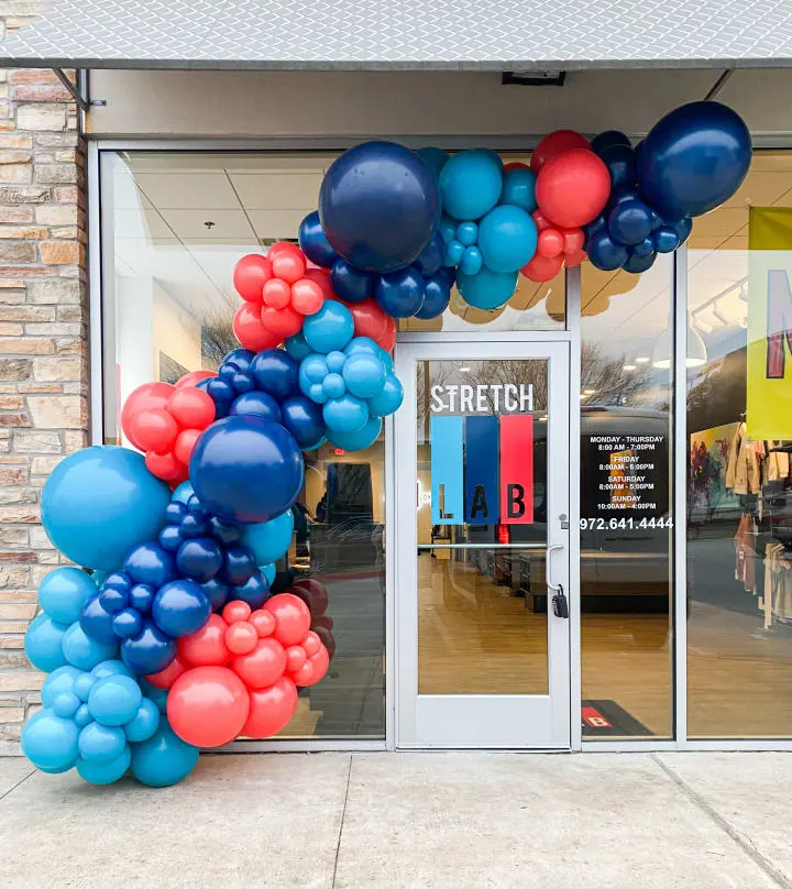 a bunch of balloons that are in front of a store front door that is decorated with a bunch of blue, red, and white balloons