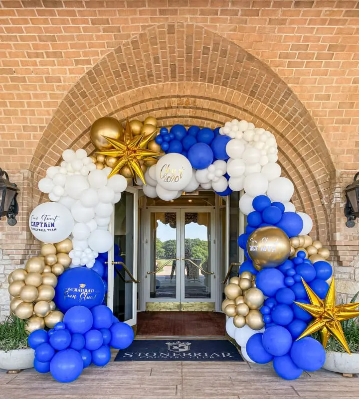 a blue and gold balloon arch with stars and balloons on the front of a brick building with a door