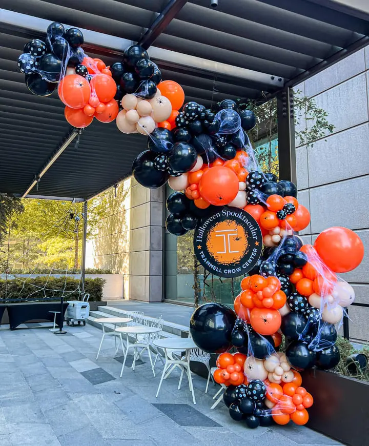 a bunch of balloons that are hanging from a pole in front of a building with tables and chairs around it