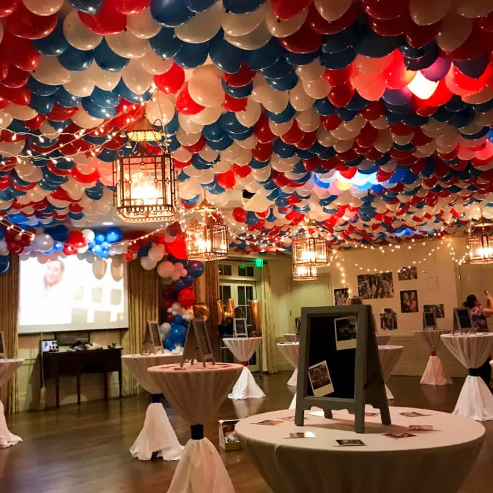 a room filled with lots of balloons and tables with white linens on the tables and a projector screen in the middle of the room