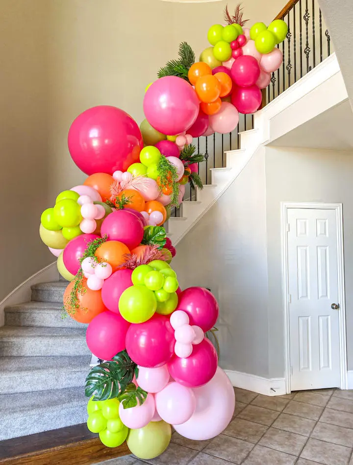 a staircase decorated with balloons and greenery for a birthday or baby's first birthday party in pink, green, orange, and pink