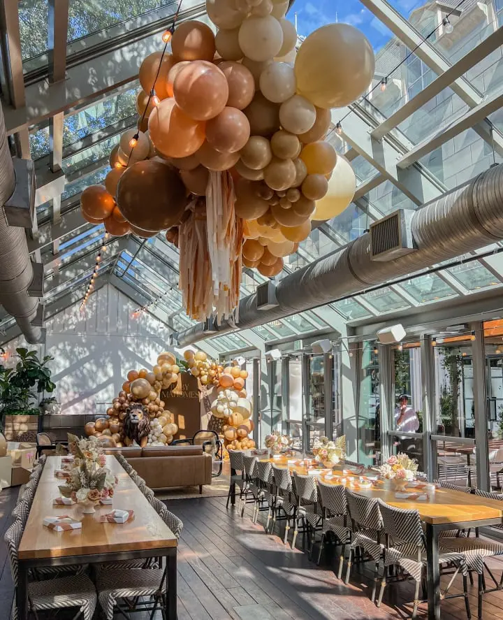 a room filled with lots of tables and chairs under a glass ceiling filled with balloons hanging from the ceiling