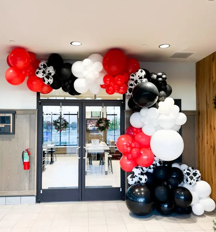 a bunch of balloons that are on the ground in front of a door that is decorated with black, white, and red balloons