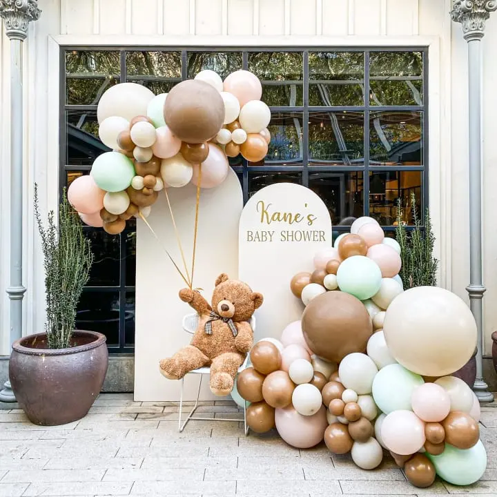 a teddy bear sitting on a chair next to a bunch of balloons in front of a baby shower sign