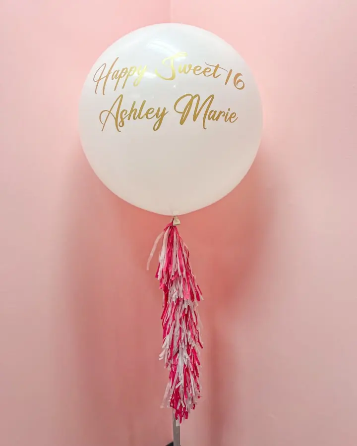 a balloon that says happy sweet 16 and a tassel of pink and white streamers hangs from a hook on a pink wall